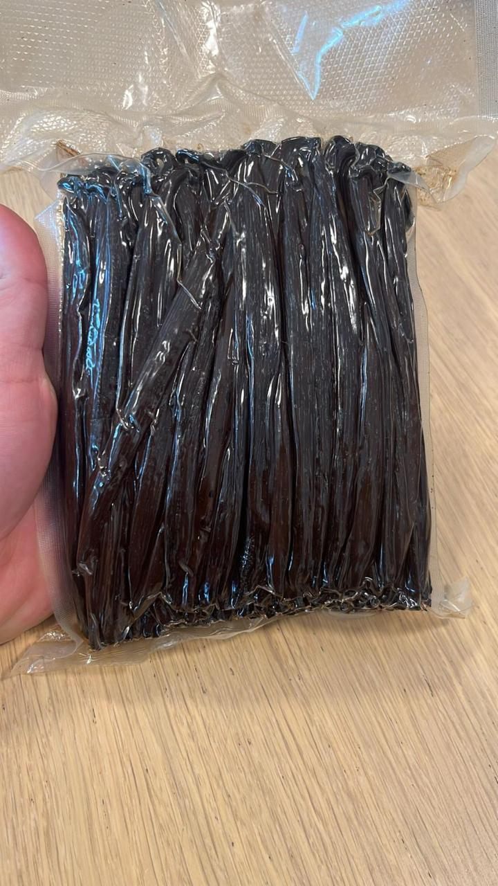 A hand holding a vacuum-sealed pack of vanilla beans, showing the size of a single retail unit